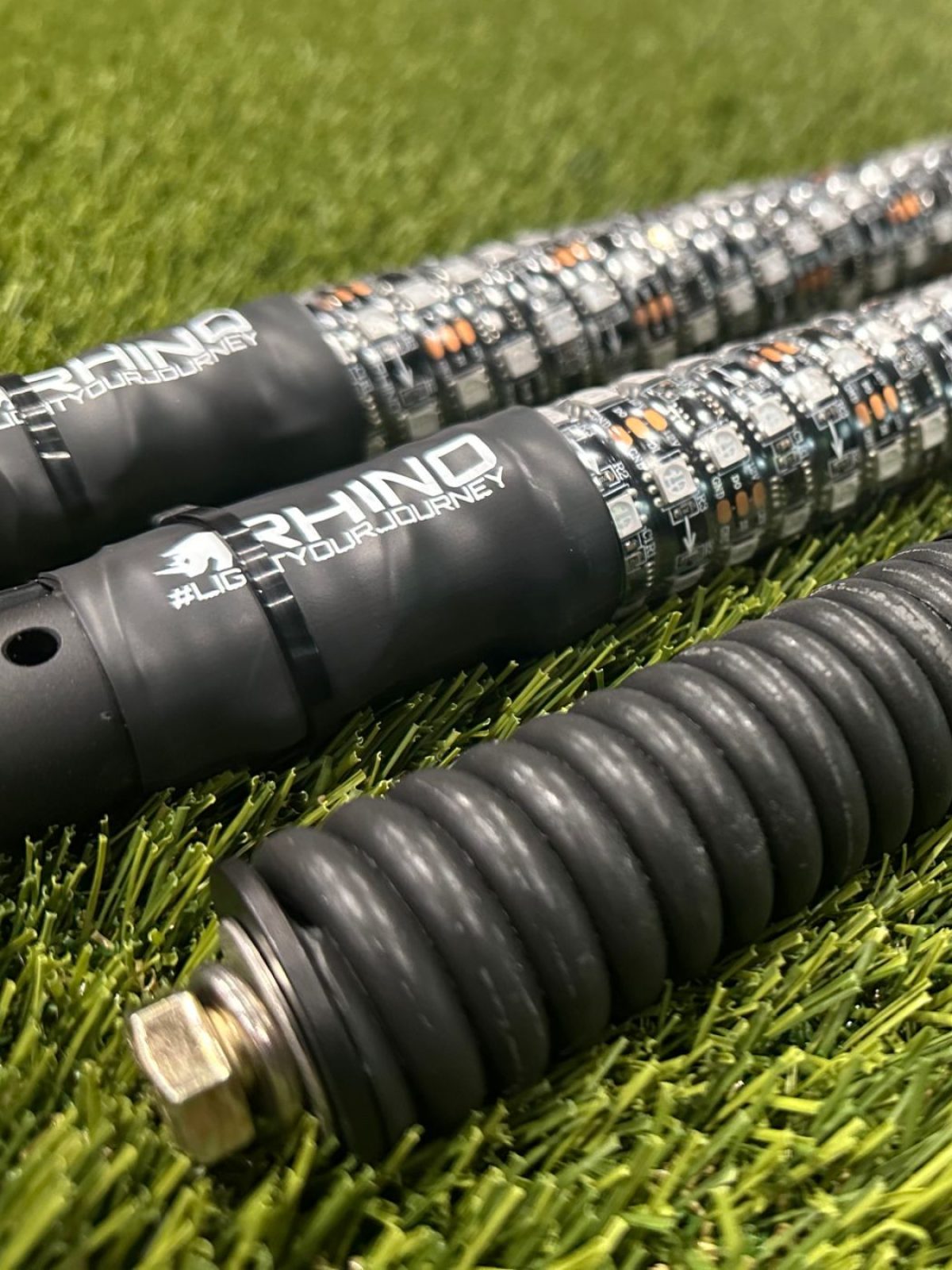 A whip and its spring base together on turf, the branded collar, the spring and the brass mounting stud all in one frame